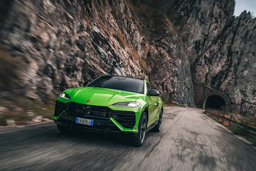 Grüner Lamborghini Urus Performante fährt dynamisch durch ein Gebirgstal