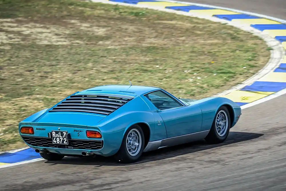 Ein hellblauer Lamborghini Miura S in einer Steilkurve – Symbol für die Ära der Supersportwagen der späten 1960er Jahre.