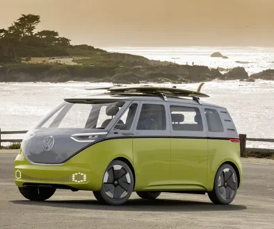 Ein lindgrüner VW ID.Buzz Concept als Elektro-Camper mit Surfbrettern auf dem Dach an der Küste – Symbol für nachhaltiges Reisen.