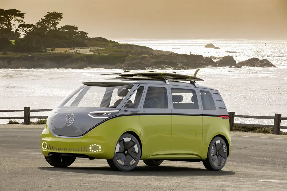 Ein lindgrüner VW ID.Buzz Concept als Elektro-Camper mit Surfbrettern auf dem Dach an der Küste – Symbol für nachhaltiges Reisen.