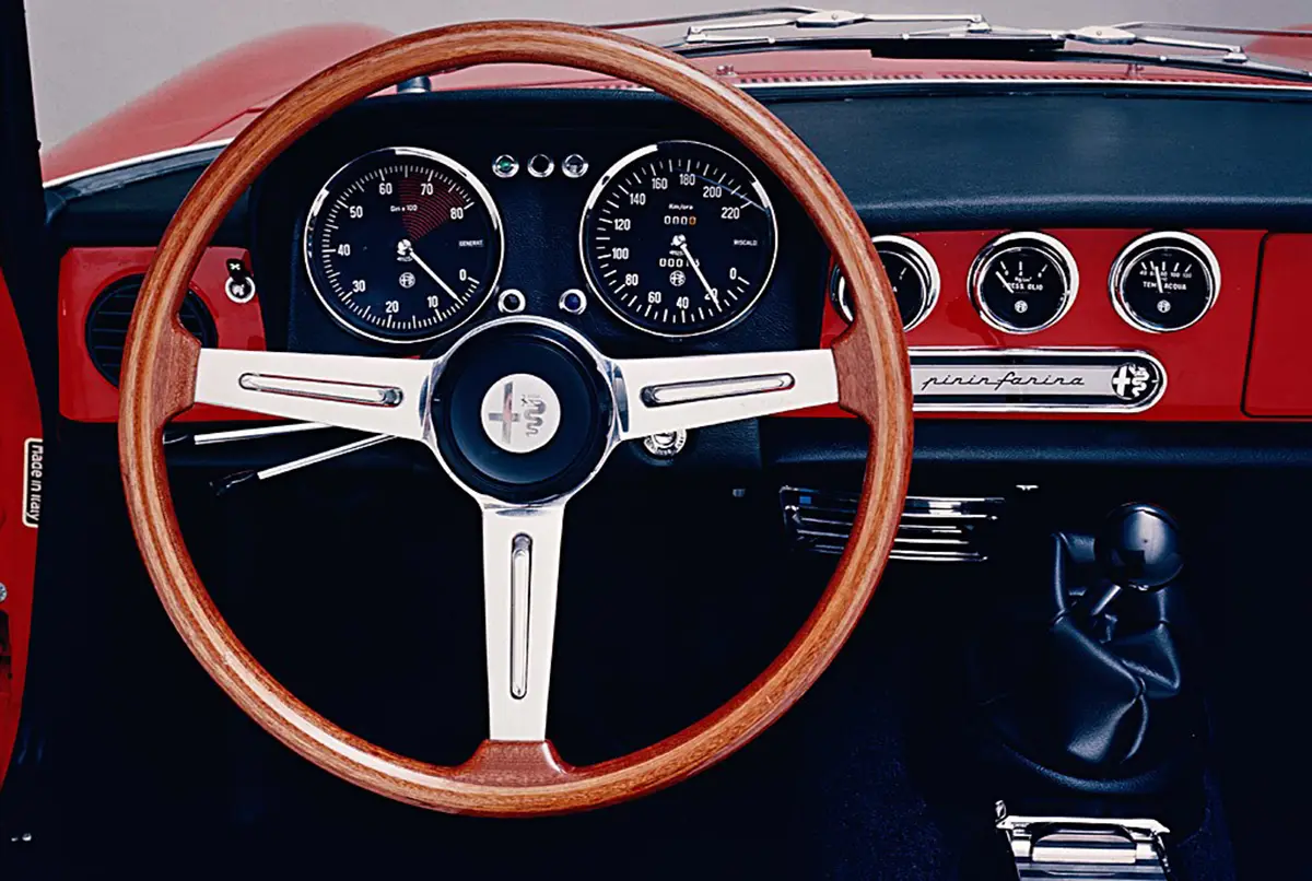 Klassisches Cockpit des Alfa Romeo Spider 1600 mit Holzlenkrad und verchromten Rundinstrumenten.