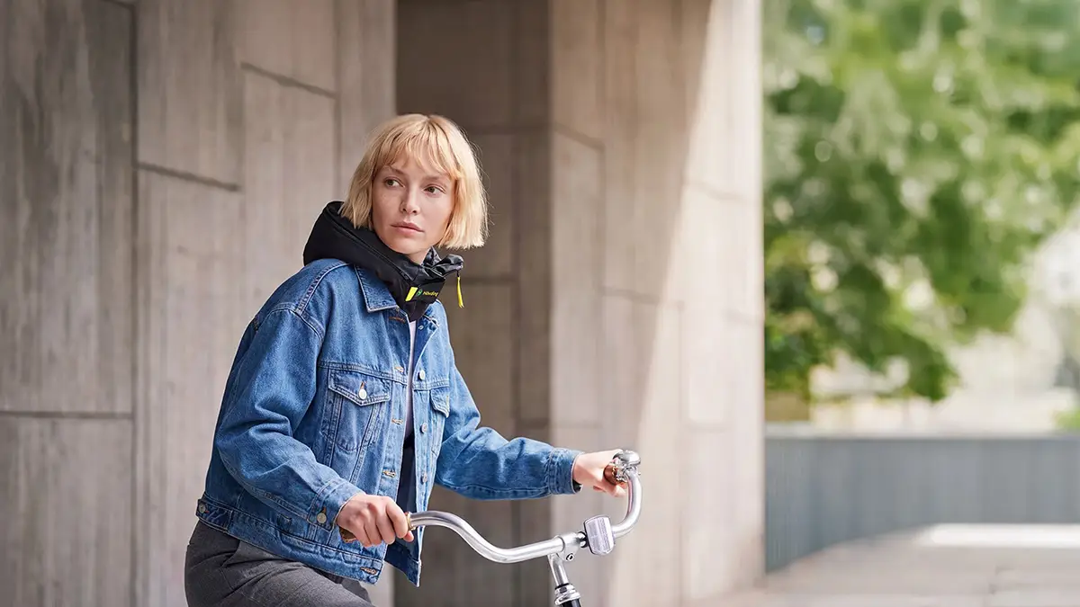 Eine Radfahrerin trägt den unauffälligen Hövding Airbag-Kragen im geschlossenen Zustand während der Fahrt im städtischen Raum.