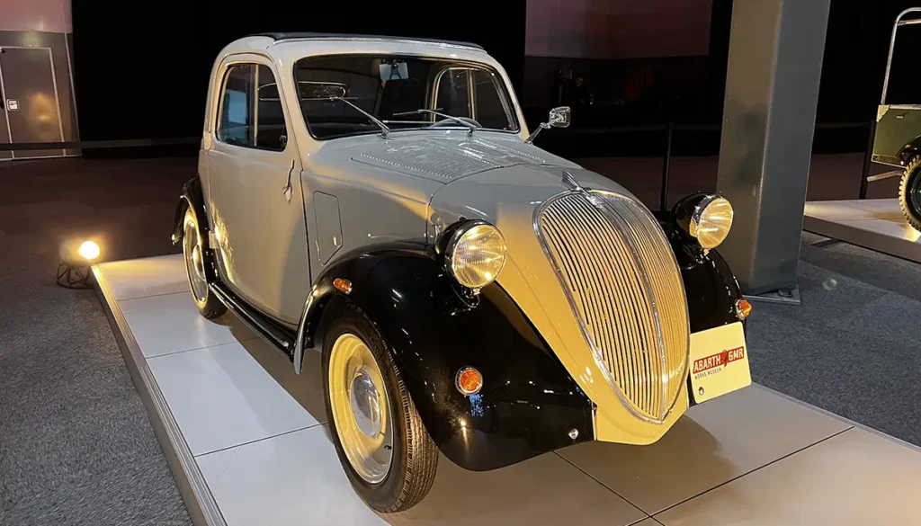 Historischer Ur-Fiat 500 Topolino von 1936 in zweifarbiger Lackierung mit schwarzen Kotflügeln und der markanten Fahrzeugfront im Werk Turin-Lingotto.
