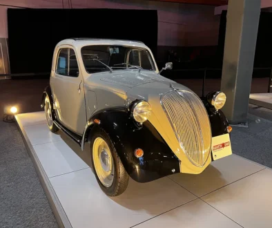 Historischer Ur-Fiat 500 Topolino von 1936 in zweifarbiger Lackierung mit schwarzen Kotflügeln und der markanten Fahrzeugfront im Werk Turin-Lingotto.