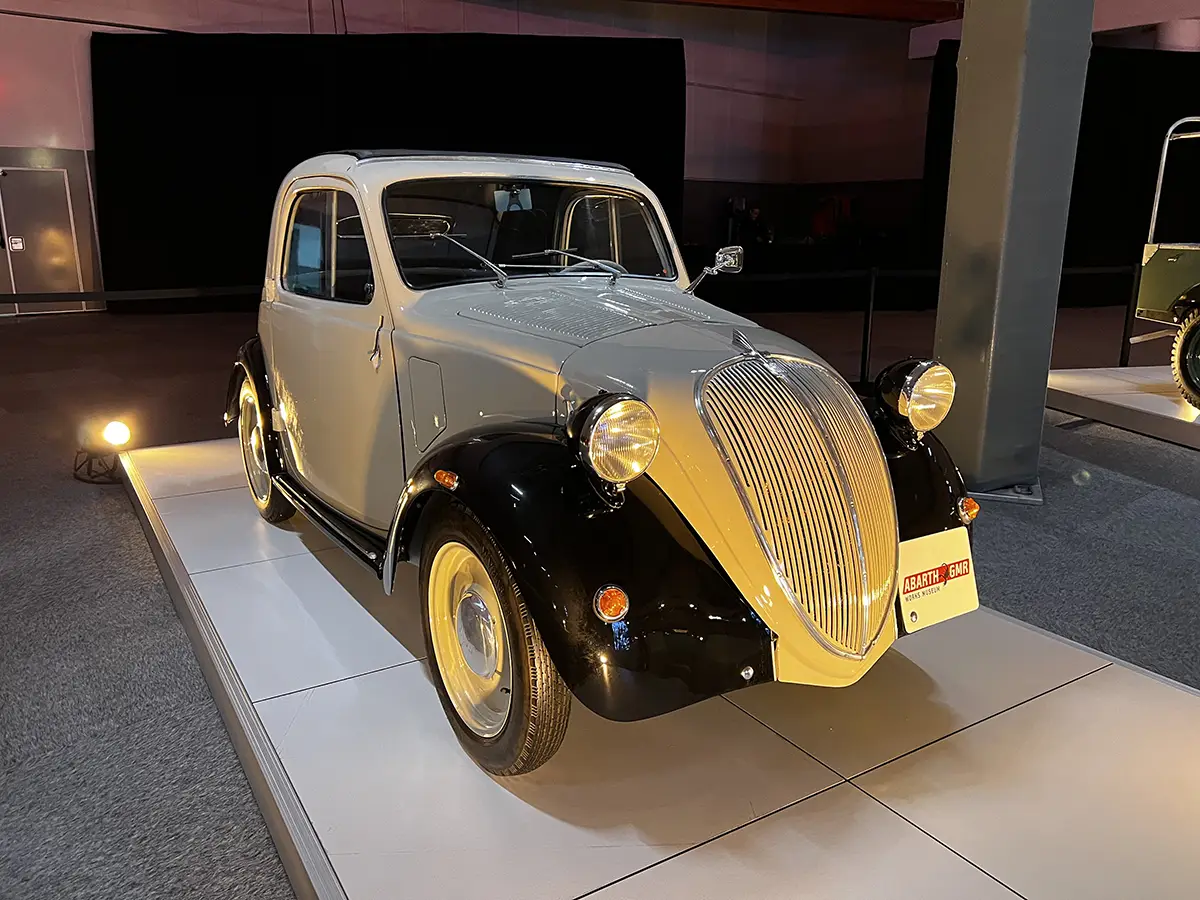 Historischer Ur-Fiat 500 Topolino von 1936 in zweifarbiger Lackierung mit schwarzen Kotflügeln und der markanten Fahrzeugfront im Werk Turin-Lingotto.