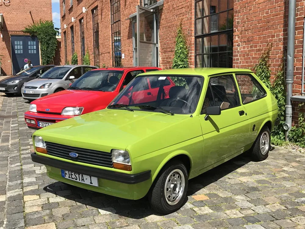 Hellgrüner Ford Fiesta der ersten Generation (1976) vor einem historischen Backsteingebäude.
