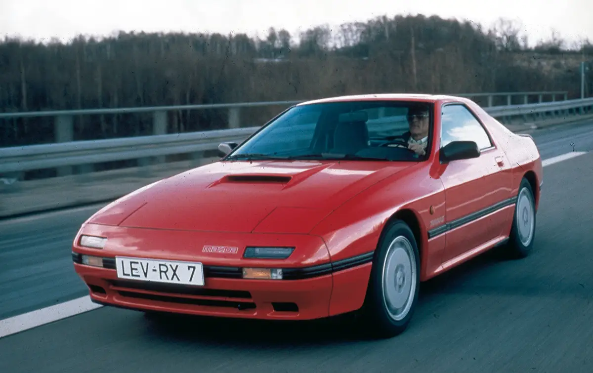 Klassisches Mazda RX-7 FC Coupé in leuchtendem Rot mit charakteristischen Klappscheinwerfern.
