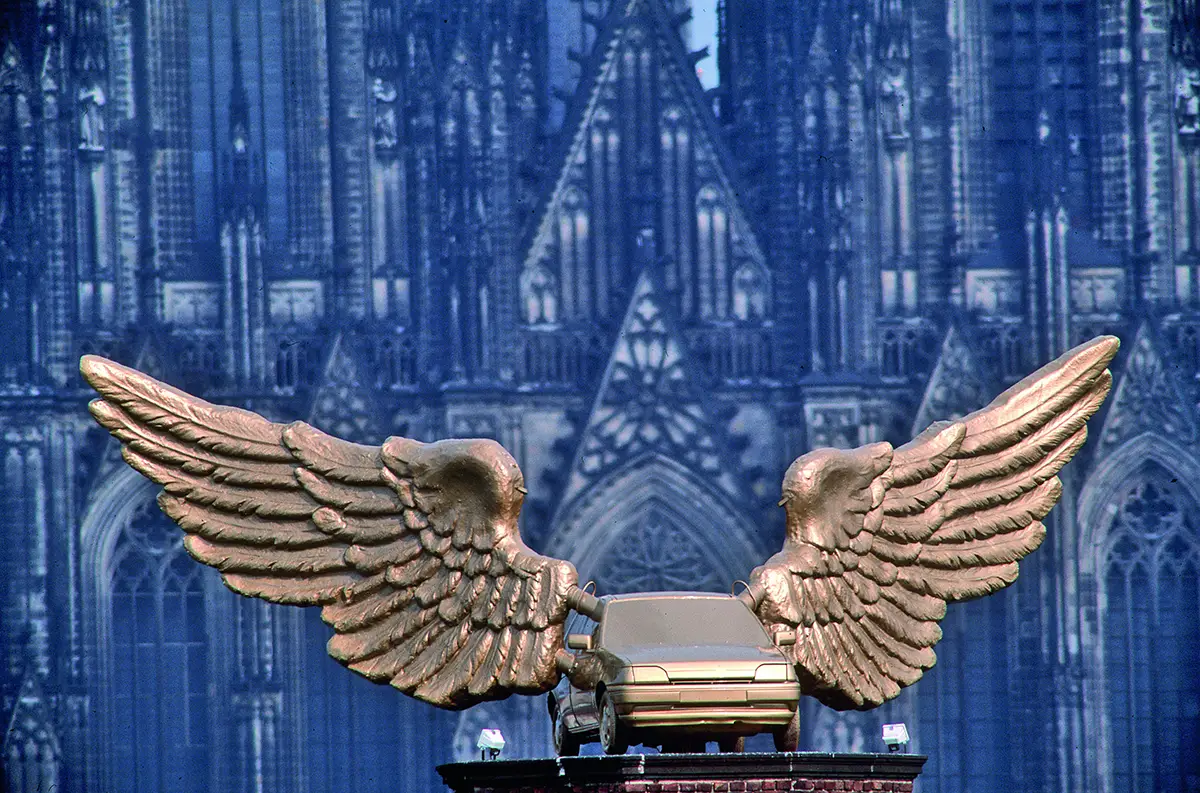 Kunstwerk „Goldener Vogel“ von HA Schult: Ein Ford Fiesta mit goldenen Flügeln vor dem Kölner Dom.