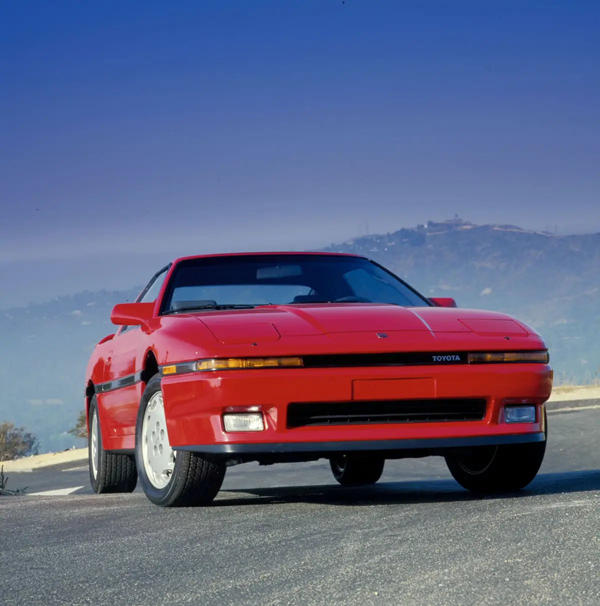 Frontansicht einer roten Toyota Supra A70 mit ausgeklappten Scheinwerfern und markantem 80er-Jahre-Design.
