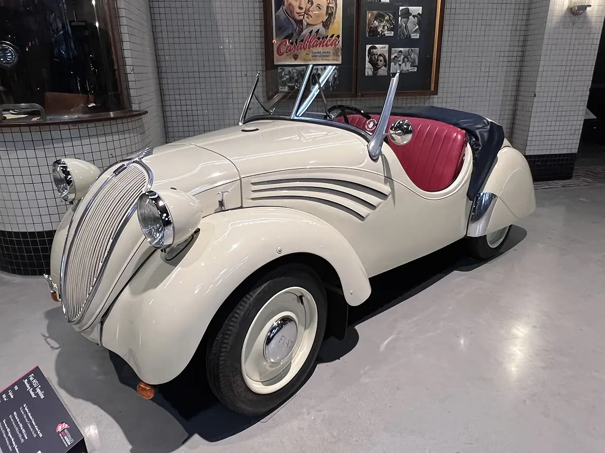Ein seltener cremeweißer NSU-Fiat 500 Topolino Roadster mit roten Ledersitzen, ausgestellt in einem Museum.