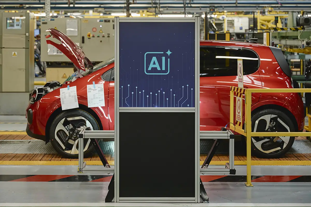 Ein roter Renault Kleinwagen in der Montagehalle vor einer teilautomatisierten Prüfstation mit einem großen blauen Display und weißem „AI“-Schriftzug für künstliche Intelligenz.
