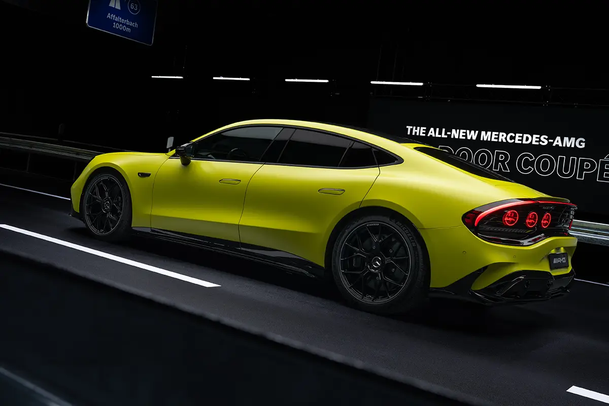 Seitenprofil des gelben Mercedes-AMG GT 4-Türer Coupés in einem abgedunkelten Tunnel mit der beleuchteten Aufschrift „THE ALL-NEW MERCEDES-AMG“ im Hintergrund.