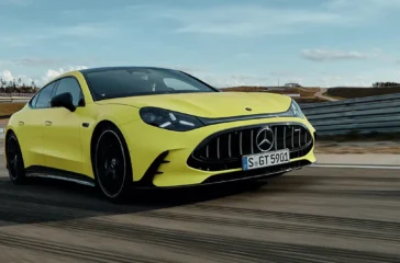 Ein sportlich-extrovertiertes, hellgelbes Mercedes-AMG GT 4-Türer Coupé in dynamischer Fahrt auf einer asphaltierten Rennstrecke unter leicht bewölktem Himmel.