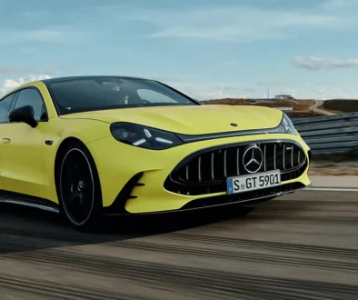 Ein sportlich-extrovertiertes, hellgelbes Mercedes-AMG GT 4-Türer Coupé in dynamischer Fahrt auf einer asphaltierten Rennstrecke unter leicht bewölktem Himmel.
