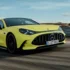 Ein sportlich-extrovertiertes, hellgelbes Mercedes-AMG GT 4-Türer Coupé in dynamischer Fahrt auf einer asphaltierten Rennstrecke unter leicht bewölktem Himmel.