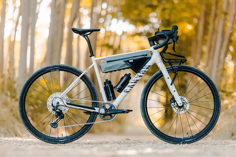 Das neue Canyon Grizl AL Gravel-Bike in Silber-Grau mit montierter Rahmentasche, zwei Trinkflaschen und einem Frontgepäckträger, perfekt in Szene gesetzt in einem herbstlichen Waldgebiet.