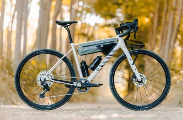 Das neue Canyon Grizl AL Gravel-Bike in Silber-Grau mit montierter Rahmentasche, zwei Trinkflaschen und einem Frontgepäckträger, perfekt in Szene gesetzt in einem herbstlichen Waldgebiet.