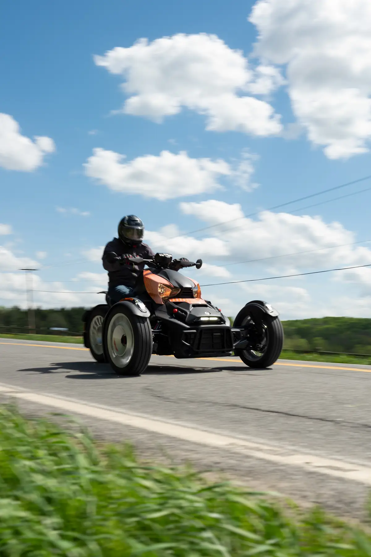 Frontalperspektive des Can-Am Ryker Rally während der Fahrt unter leicht bewölktem Himmel, die das breite Fahrwerk der beiden Vorderräder und den markanten Kühler betont.