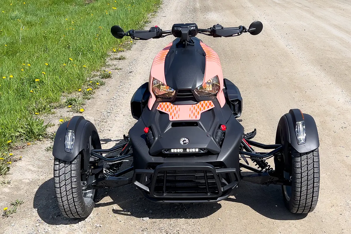 Frontalansicht des stehenden Can-Am Ryker Rally Dreirads auf einem unbefestigten Weg zur Veranschaulichung der markanten Frontoptik und der Reifenbreite.