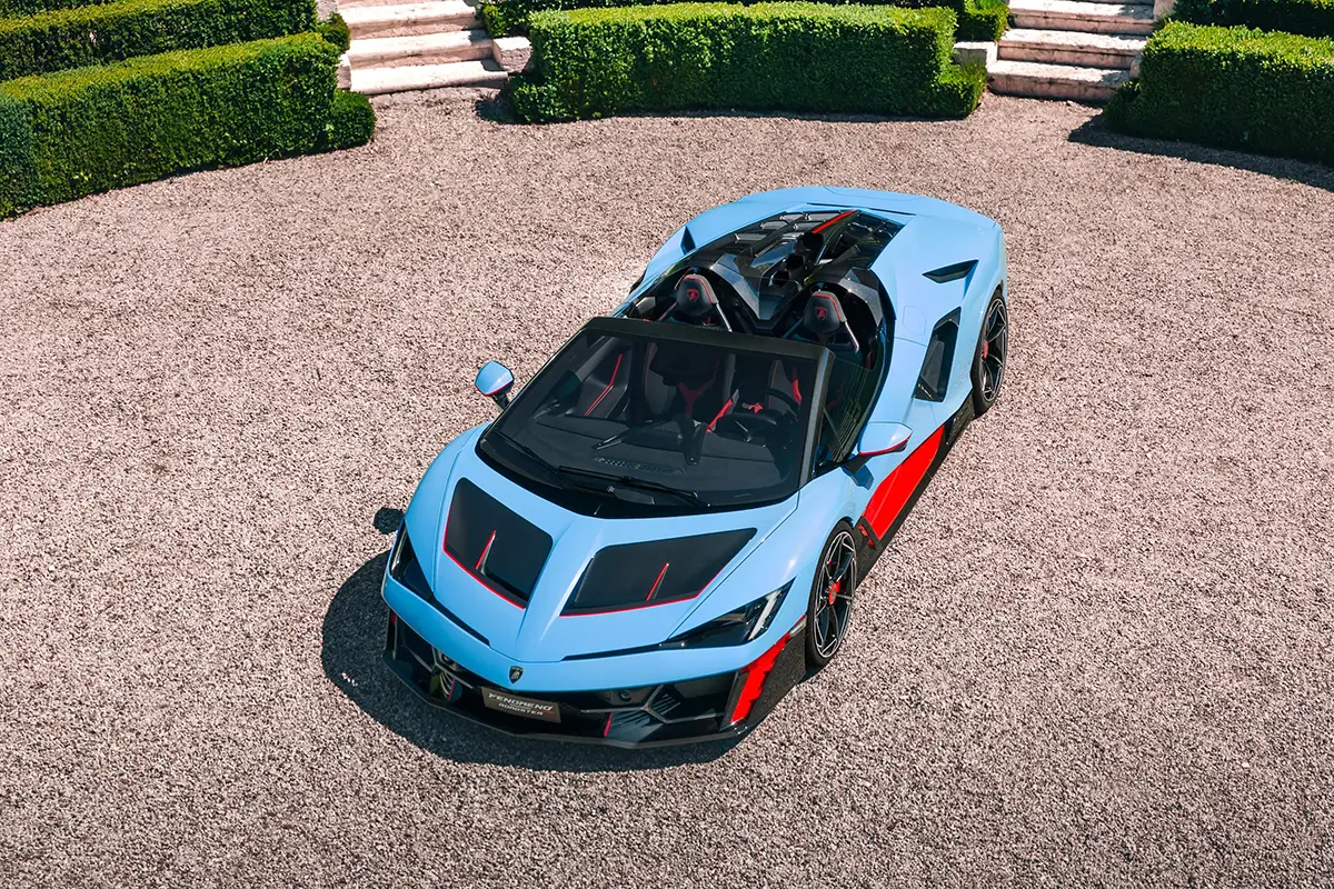Frontalansicht des hellblauen Fenomeno Roadster vor einer mediterranen Gartenkulisse.