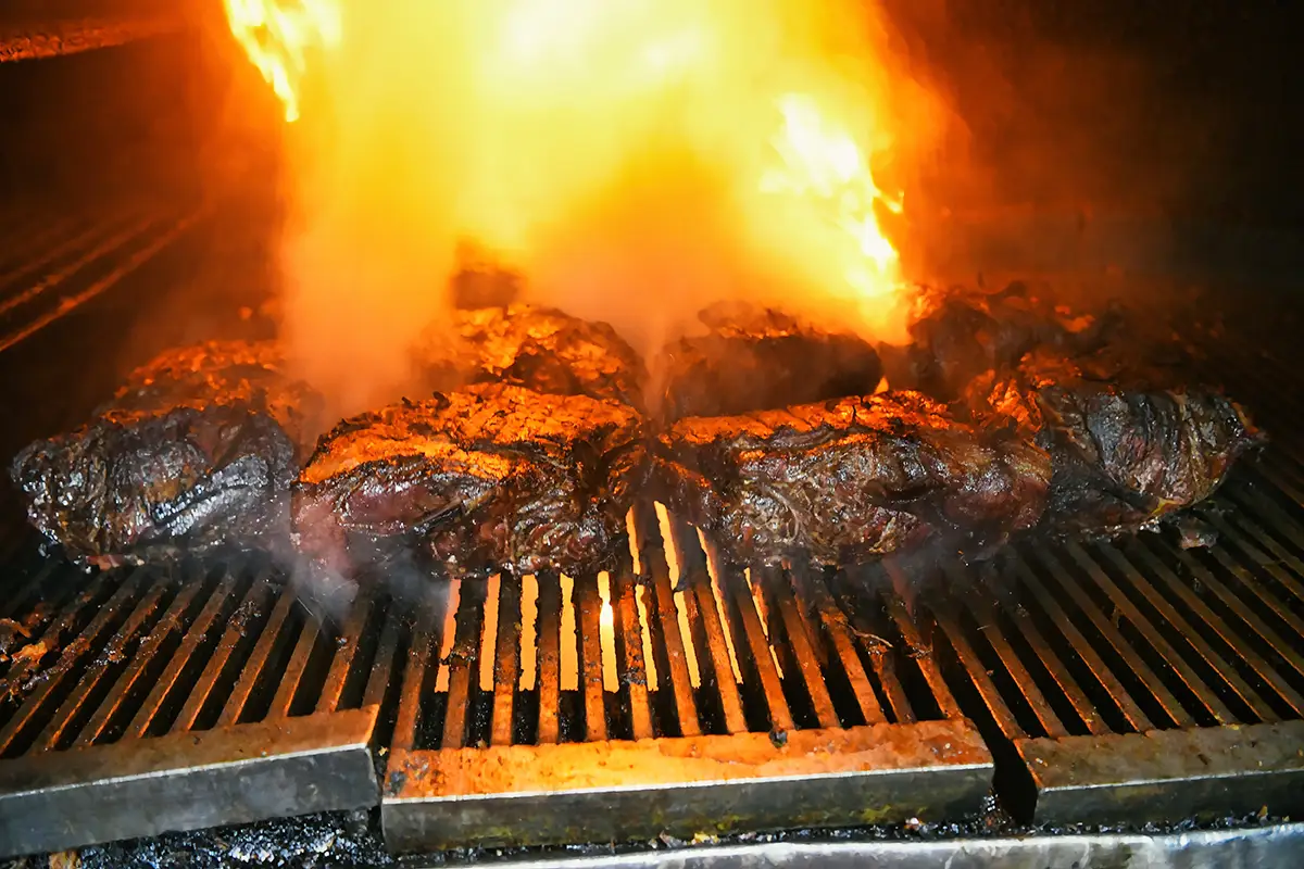 Saftige Fleischrippchen (Ribs) brutzeln auf einem großen Barbecue-Grill über offener, auflodernder Flamme.