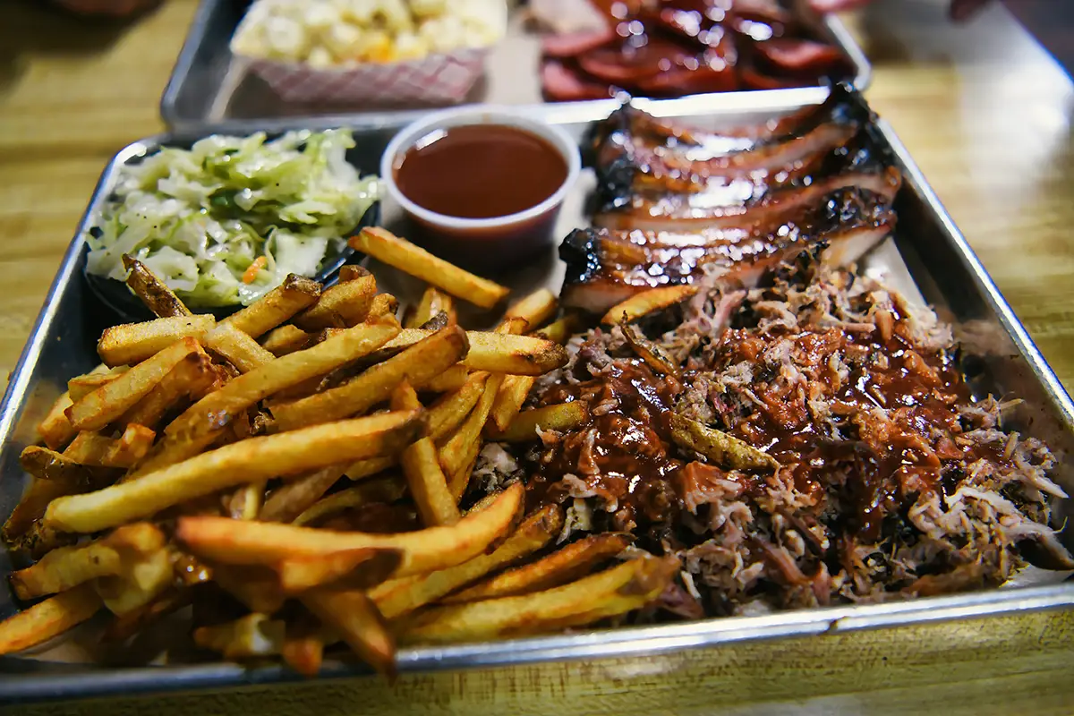 Eine gefüllte Servierschale mit typisch amerikanischem BBQ: Pommes Frites, Coleslaw-Salat, Sauce und zart gegrilltes Fleisch.