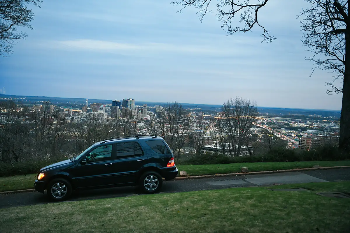 Seitenansicht eines dunklen Mercedes ML Geländewagens, geparkt auf einer Anhöhe mit Panoramablick auf die Stadt Tuscaloosa im Hintergrund.