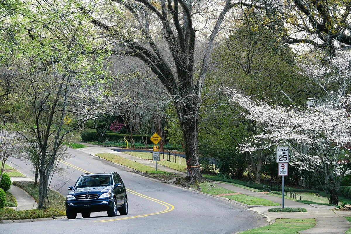 Ein schwarzer Mercedes ML SUV fährt eine idyllische, von grünen Bäumen und blühenden weißen Büschen gesäumte Straße in Alabama entlang.