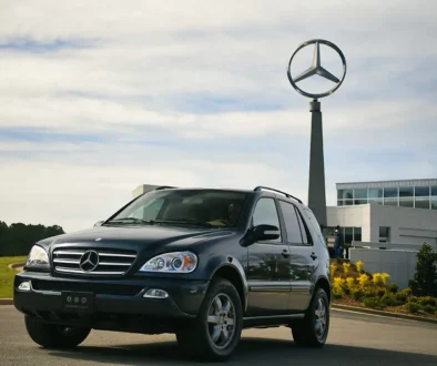 Ein klassischer, dunkler Mercedes-Benz ML vor dem Hauptgebäude von Mercedes-Benz US International in Tuscaloosa mit dem großen, hoch aufragenden Mercedes-Stern im Hintergrund.