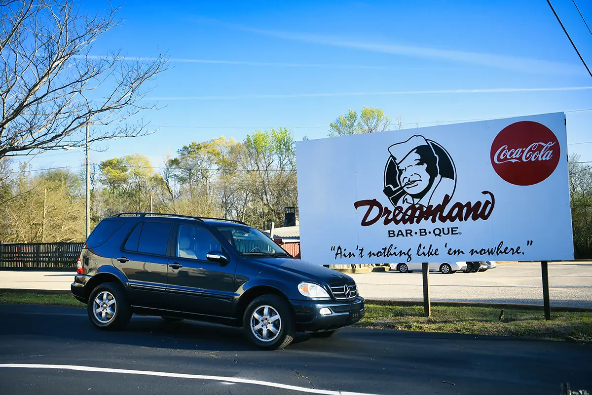 Der Mercedes ML parkt am Straßenrand vor dem großen, weißen Werbeschild des bekannten Restaurants Dreamland Bar-B-Que.