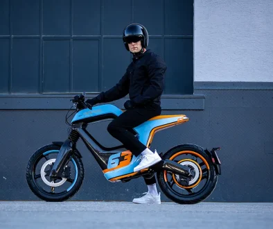 Seitenansicht des Novus One Elektro-Motorrads in Blau-Orange mit Fahrer zur Demonstration der Sitzposition.