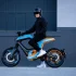 Seitenansicht des Novus One Elektro-Motorrads in Blau-Orange mit Fahrer zur Demonstration der Sitzposition.