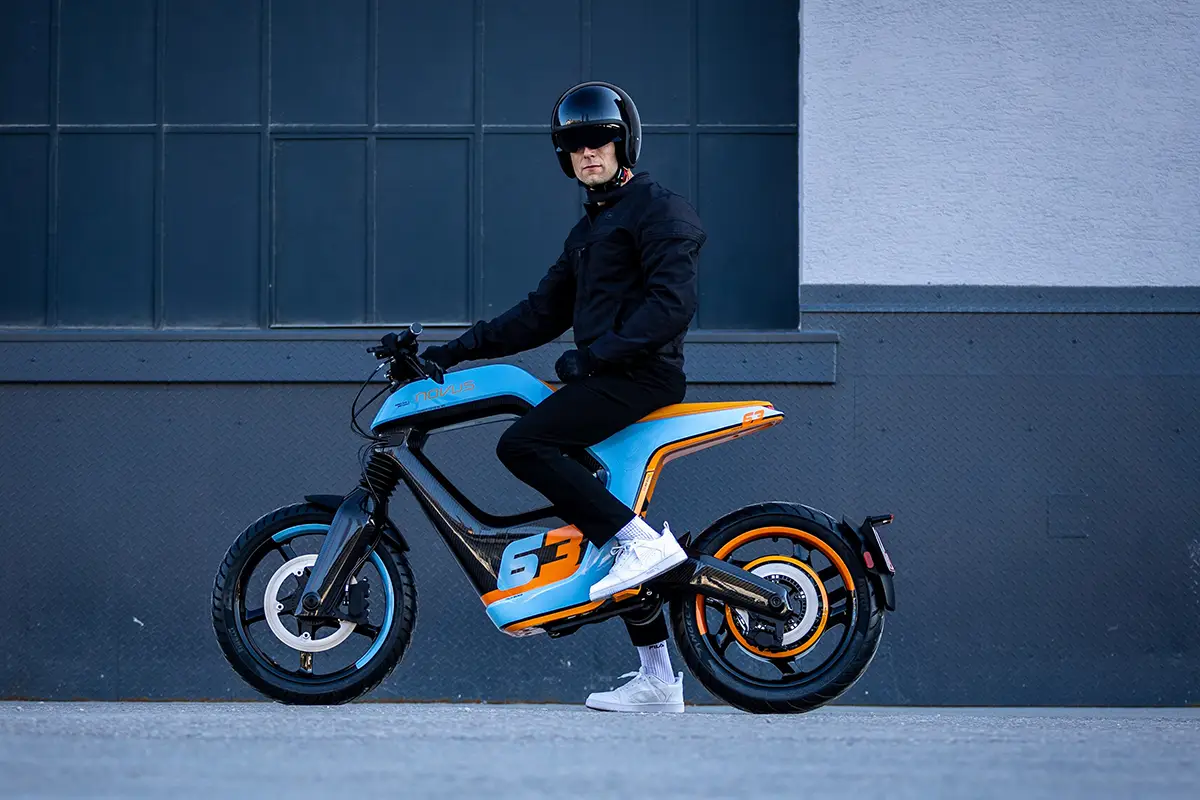 Seitenansicht des Novus One Elektro-Motorrads in Blau-Orange mit Fahrer zur Demonstration der Sitzposition.