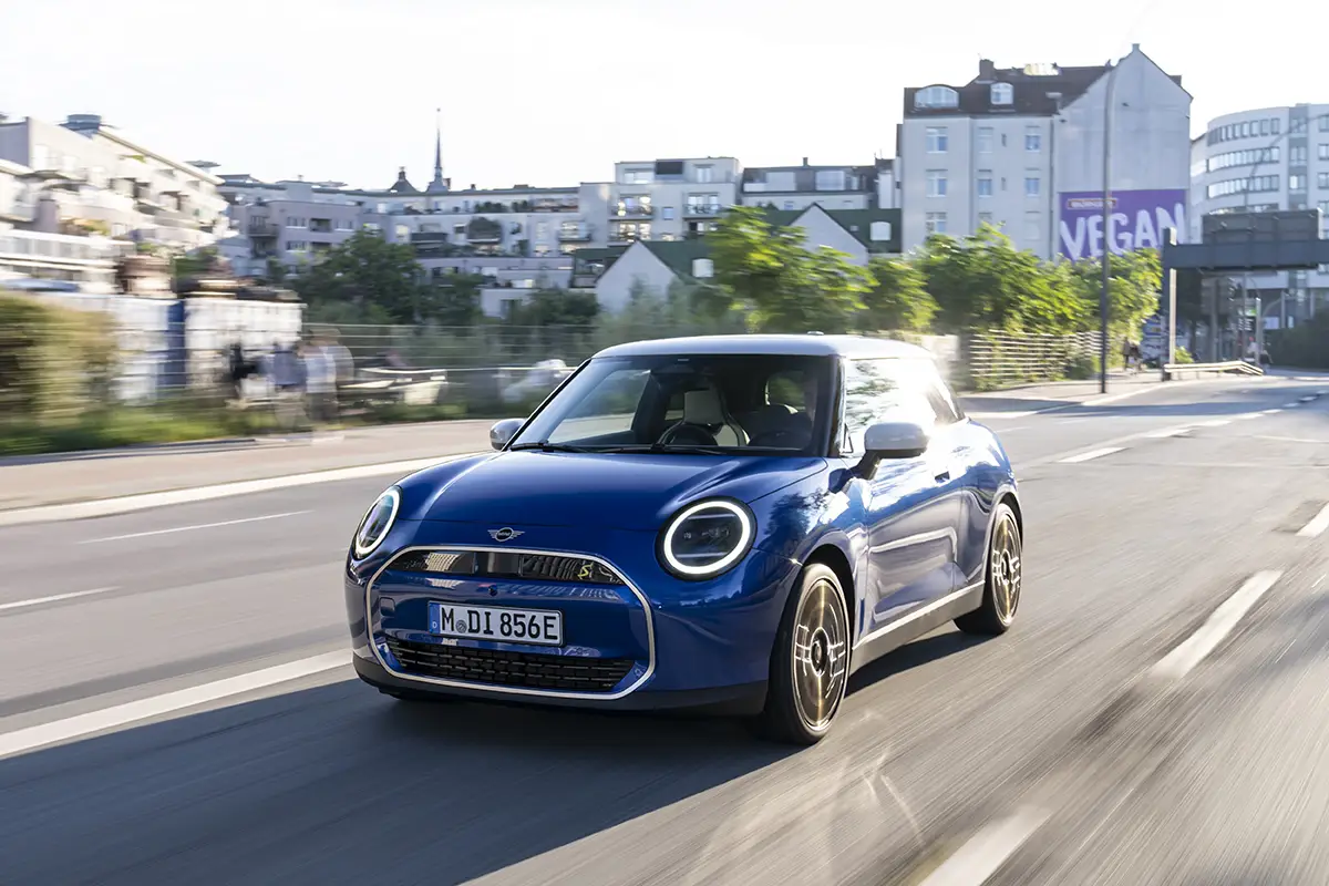 Blauer Mini Cooper Electric bei der Fahrt durch ein urbanes Wohngebiet.