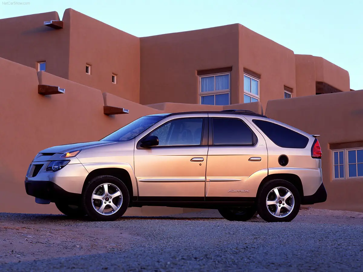 Ein Pontiac Aztek Crossover-SUV in Silber vor einer modernen Wohnhaus-Kulisse, bekannt für sein ungewöhnlich kantiges und zerklüftetes Karosseriedesign.