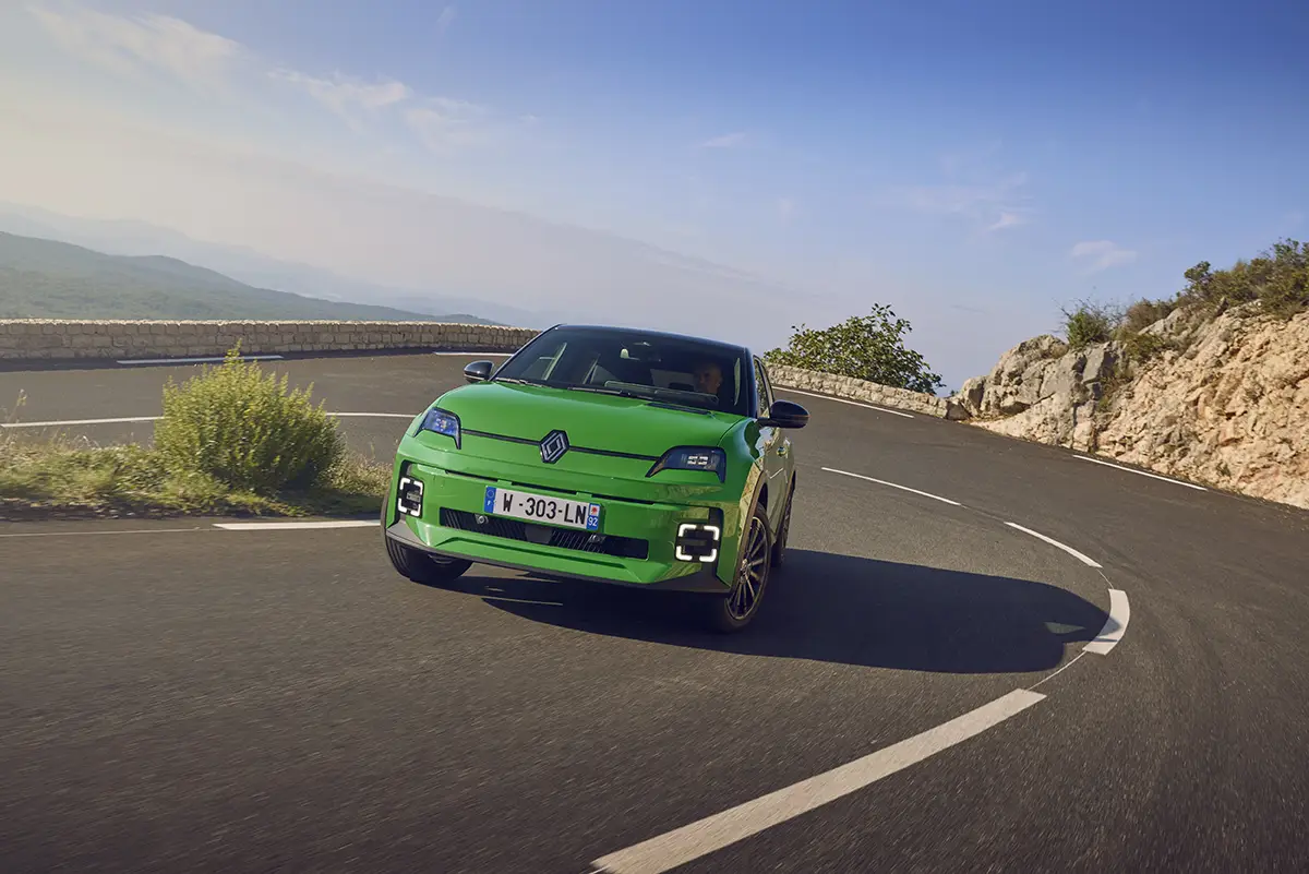 Grüner Renault 5 E-Tech in einer dynamischen Kurvenfahrt auf einer Bergstraße.