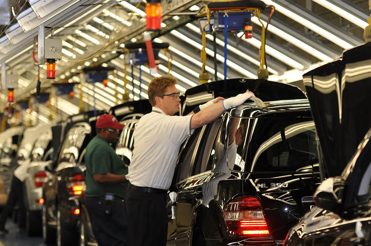 Blick in die Produktionshalle des Mercedes-Werks in Alabama, wo Fabrikarbeiter am Fließband die Karosserie schwarzer SUVs montieren.