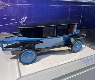 Ein historisches, blaues Modell des Rumpler Tropfenwagens aus den 1920er-Jahren, dessen stromlinienförmige Karosserie exakt der aerodynamischen Form eines fallenden Wassertropfens nachempfunden ist.