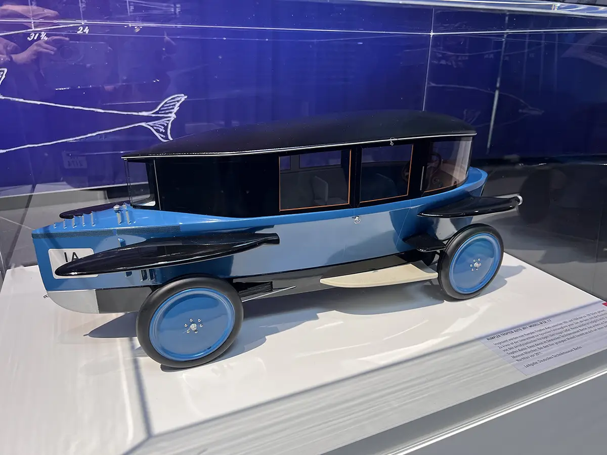 Ein historisches, blaues Modell des Rumpler Tropfenwagens aus den 1920er-Jahren, dessen stromlinienförmige Karosserie exakt der aerodynamischen Form eines fallenden Wassertropfens nachempfunden ist.