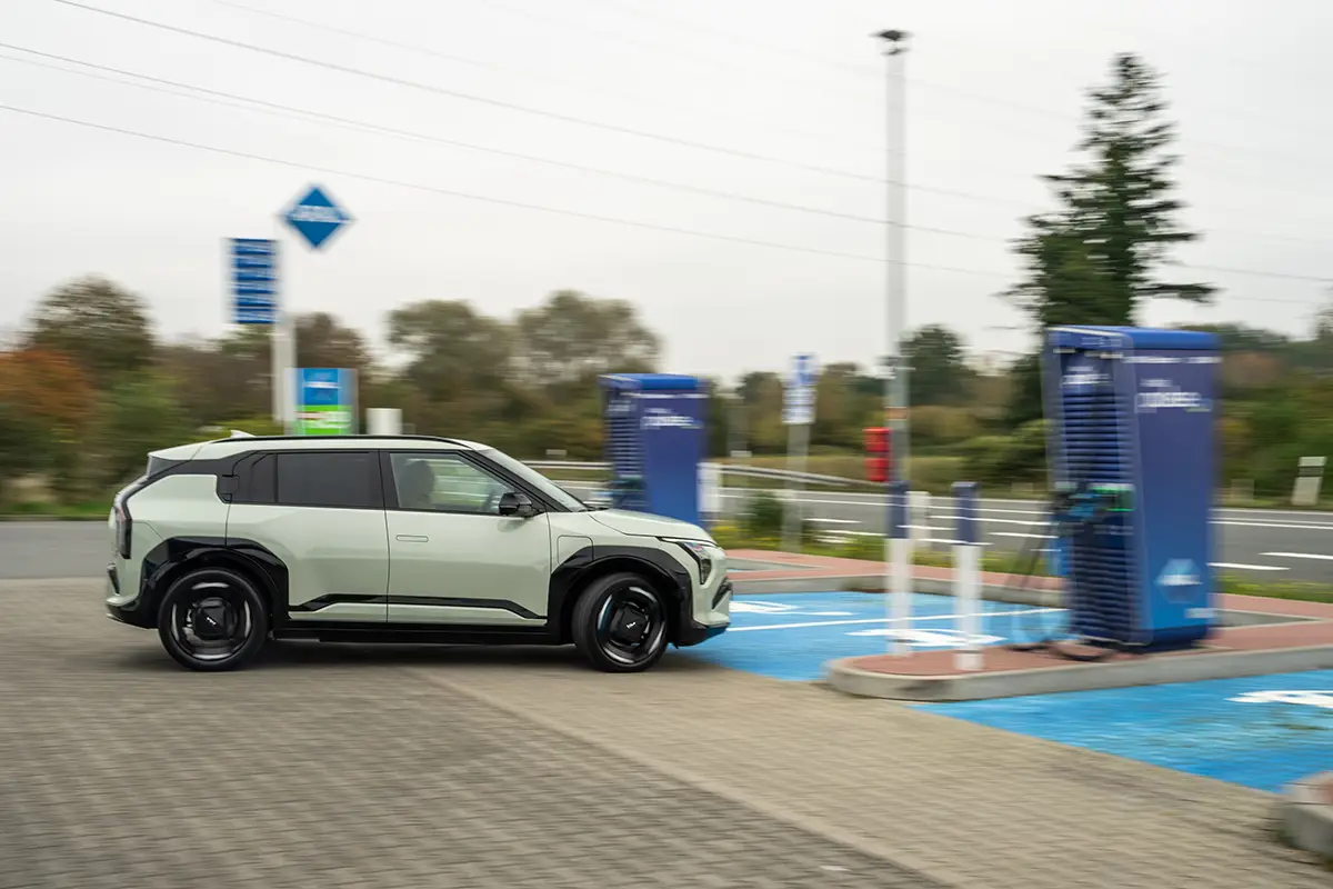 Ein weisses Elektro-SUV steht auf einem blau markierten E-Auto-Parkplatz an einer modernen Schnellladestation auf einer mitteleuropäischen Raststätte.