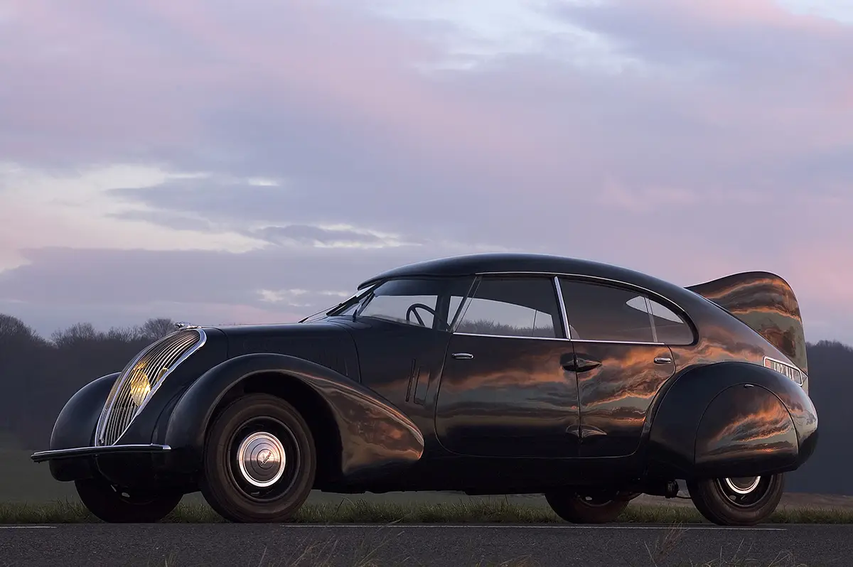 Die Seitenansicht des tiefschwarzen Peugeot 402 Andreau aus dem Jahr 1936, der mit einer markanten, flugzeugähnlichen Heckfinne für maximale Aerodynamik sorgt.