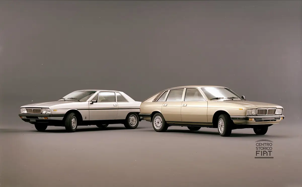 Profilansicht eines Lancia Gamma Coupés und einer Lancia Gamma Limousine nebeneinander vor grauem Studiohintergrund.