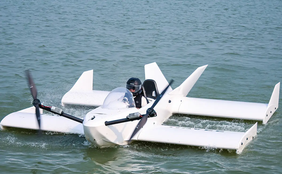 Das weiße, aus Carbon gefertigte Bodeneffektfahrzeug Navee WaveFly 5X mit zwei großen elektrischen Bug-Rotoren gleitet bei einem Testflug knapp über der Wasseroberfläche.
