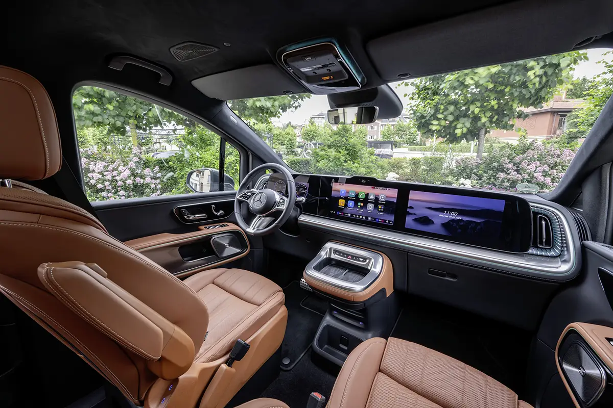 Das luxuriöse Interieur des Mercedes VLE Cockpits von vorne mit braunen Ledersitzen, Sportlenkrad und der flächendeckenden Glasfront des optionalen MBUX Superscreens.
