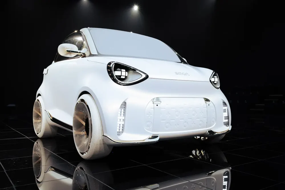 Frontalperspektive des neuen, rein weissen Smart #2 Konzeptfahrzeugs mit der modernen Lichtsignatur der Marke und weit aussen sitzenden Rädern auf einer spiegelnden schwarzen Fläche