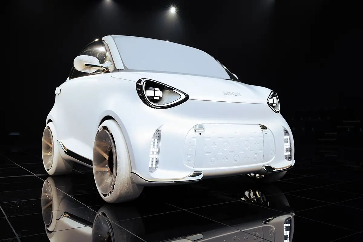 Frontalperspektive des neuen, rein weissen Smart #2 Konzeptfahrzeugs mit der modernen Lichtsignatur der Marke und weit aussen sitzenden Rädern auf einer spiegelnden schwarzen Fläche