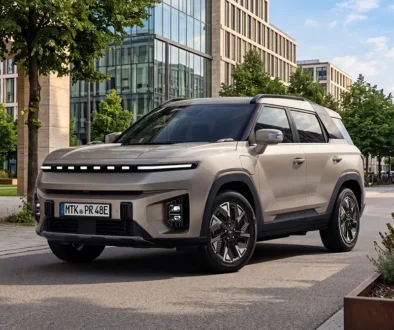 Das neue vollelektrische SUV KGM Torres EVX Nomad in elegantem Silber-Metallic parkt am Strassenrand einer modernen städtischen Allee vor einer gläsernen Bürogebäudefassade.