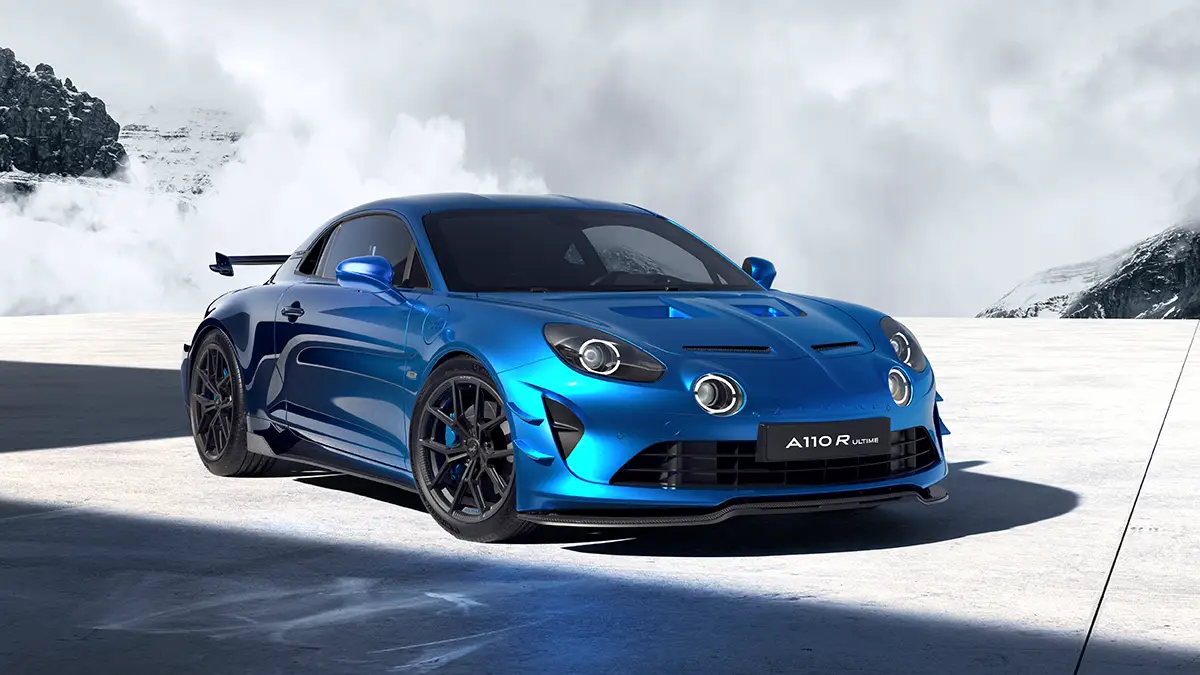 Frontalperspektive einer blauen Alpine A110 R Ultime mit aerodynamischen Carbon-Komponenten und Frontsplitter vor einer kontrastierenden Kulisse aus hellen Wolken und schneebedeckten Berggipfeln. Foto: Alpine