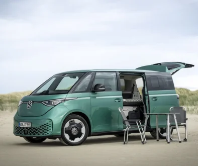 Ein minzgrüner VW ID. Buzz steht mit geöffneter Heckklappe und offener Schiebetür in einer Dünenlandschaft als kompakter Weekender.
