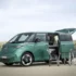 Ein minzgrüner VW ID. Buzz steht mit geöffneter Heckklappe und offener Schiebetür in einer Dünenlandschaft als kompakter Weekender.